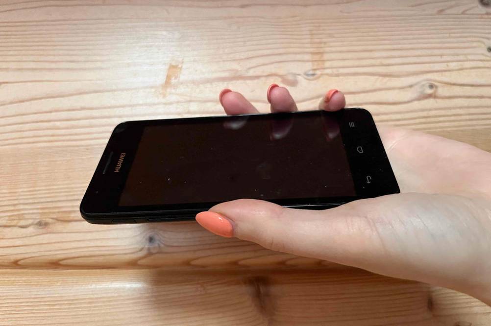 Eine Hand hält das getestete China-Handy vor eine Holzfläche.