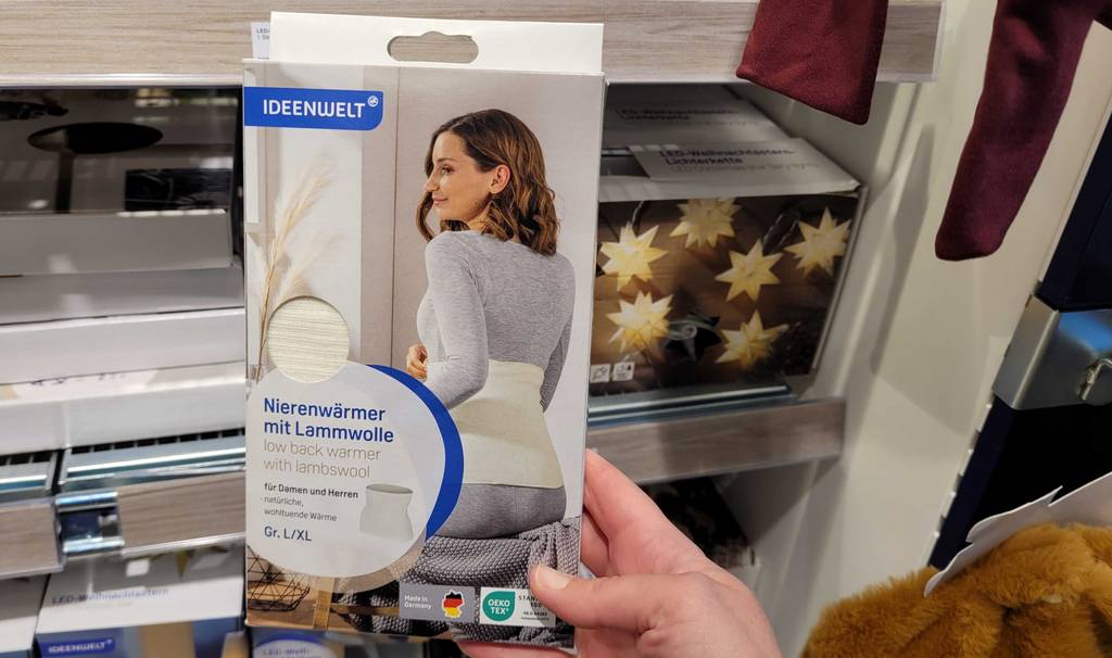 Im Test: Eine Hand hält einen verpackten Nierenwärmer vor ein Regal.