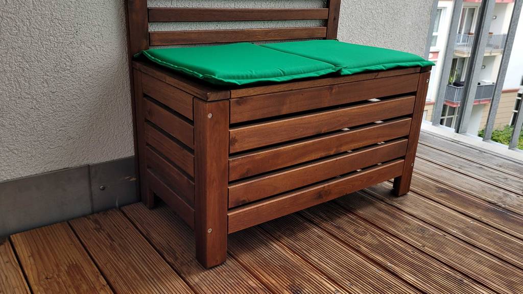 Gartenbank aus Holz mit Stauraum steht vor einer weißen Wand