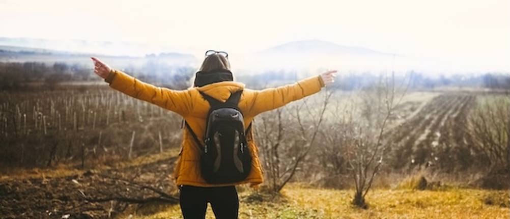 3-in-1-Jacke für Damen getestet: Eine Frau mit Wanderjacke und Rucksack von hinten mit ausgebreiteten Armen.