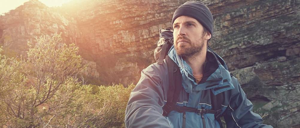 3-in-1-Jacke-Herren-Test: Ein Mann mit einer Funktionsjacken, Mütze und Rucksack in der Natur. 