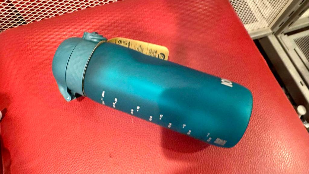 Eine getestete Kunststoff-Trinkflasche mit Skala in Blau liegt auf einem roten Gegenstand.
