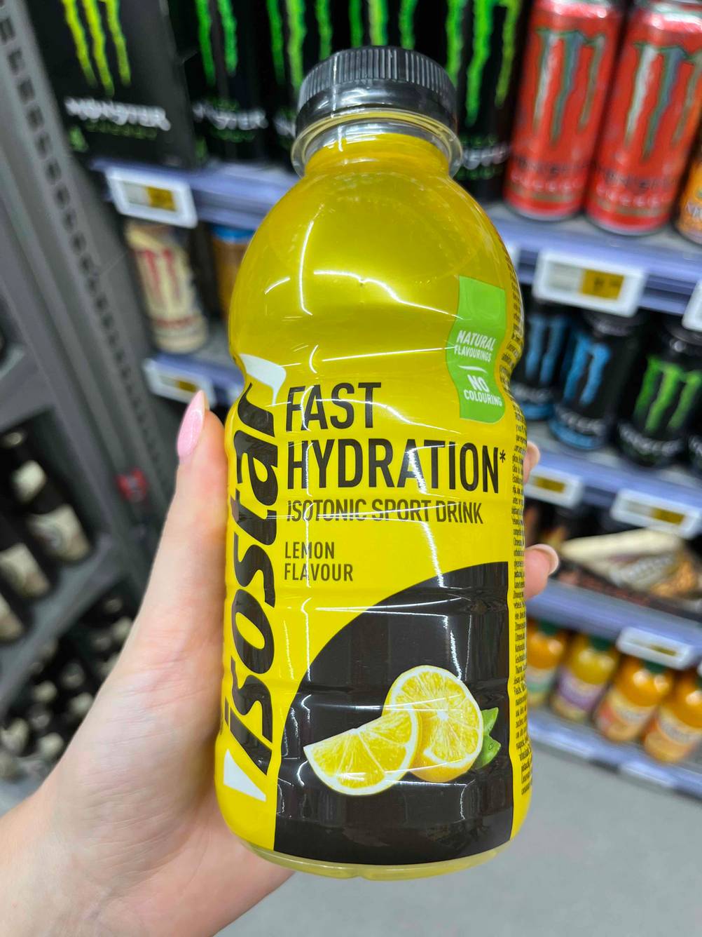 Isotonische Getränke im Test: Eine Hand hält eine Flasche Isotonisches Getränk vor ein Regal