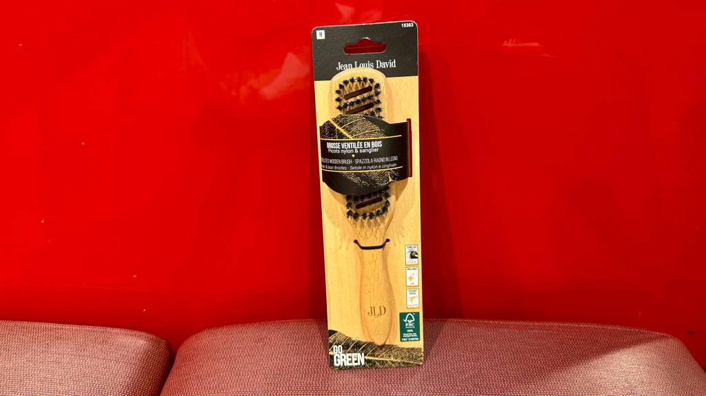 Test: Eine Holz-Haarbürste lehnt in der Verpackung an einer roten Wand.