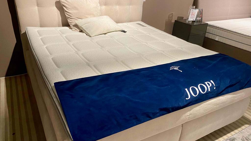 Kaltschaum-Topper getestet: ein Kaltschaum-Topper liegend auf einem Bett mit einer Schutzfolie der Marke Joop darauf.