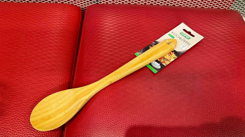 Der getestete Holz-Kochlöffel, der an einem Etikett fixiert ist liegt auf einem roten Hocker.