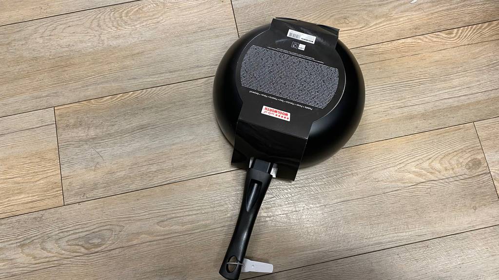 Pfanne-26cm getestet: schwarze Pfanne in Schwarz noch eingepackt liegt auf einem Boden.