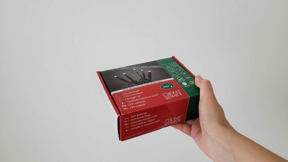 Eine Hand hält eine Packung der getesteten LED-Weihnachtsbeleuchtung vor eine helle Wand.