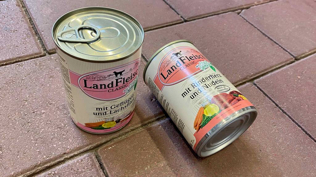 Zwei getestete LandFleisch-Hundefutter-Dosen liegen auf einem roten Steinboden