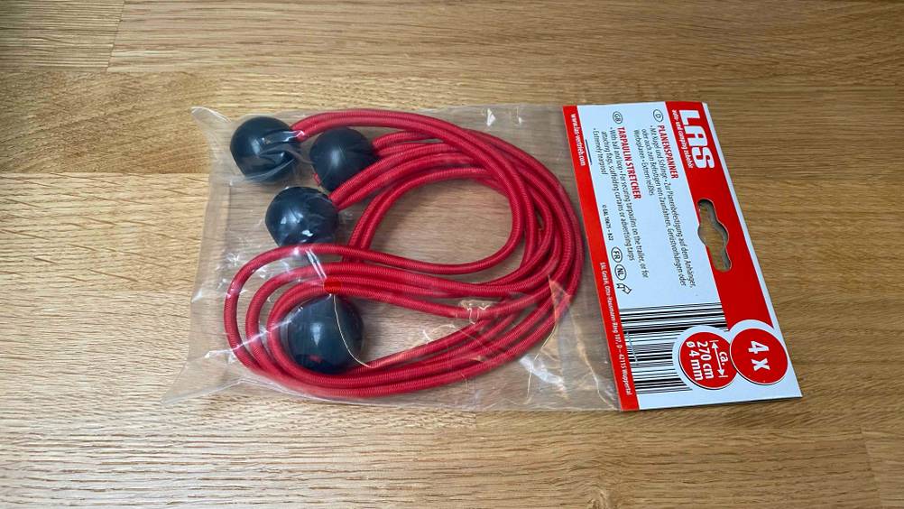 Ein getesteter Expander liegt in seiner Verpackung auf einem Holzboden.