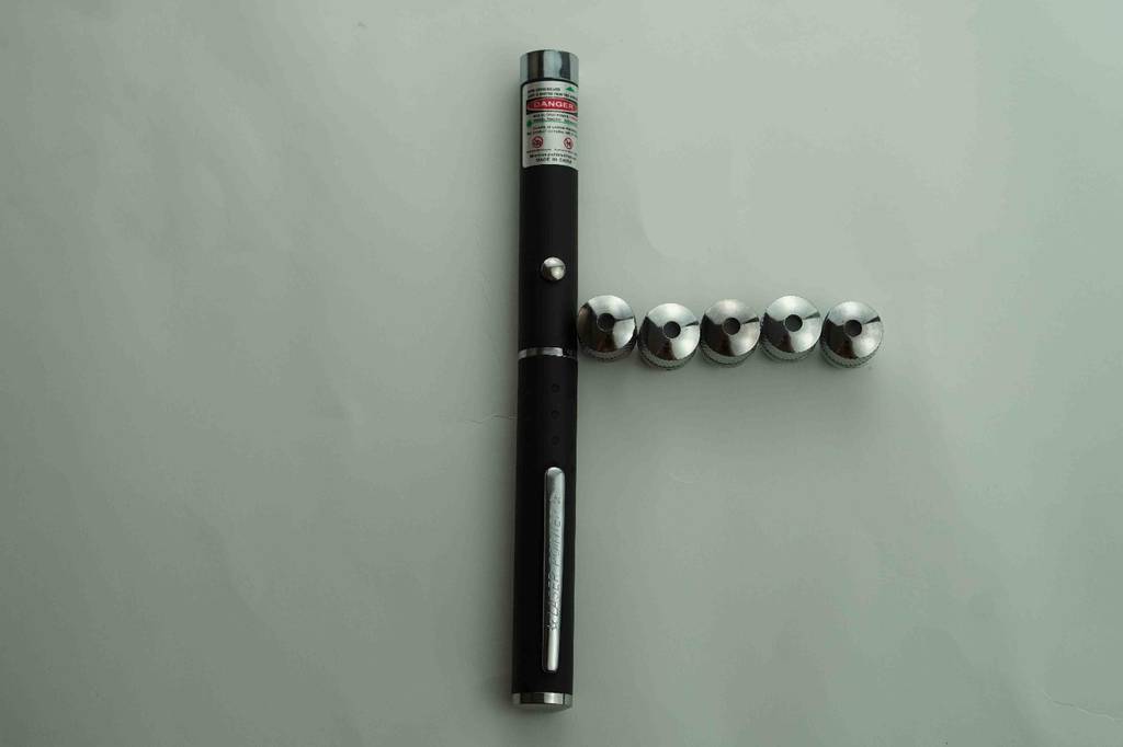 Laserpointer im Test: schwarzer Laserpointer mit verschiedenen Aufsätzen auf einer Fläche liegend.