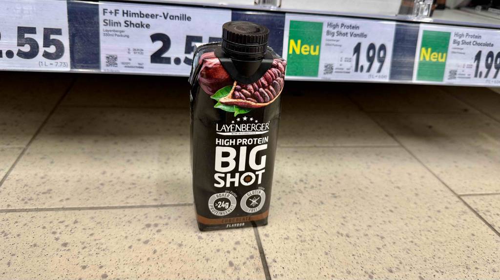 Der getestete Eiweißdrink mit 24 g Eiweiß, steht vor einem Regal.