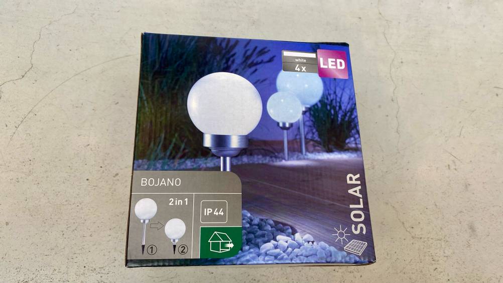 Auf einem hellen Betonboden liegt eine getestete Solarkugel in ihrer Verpackung.