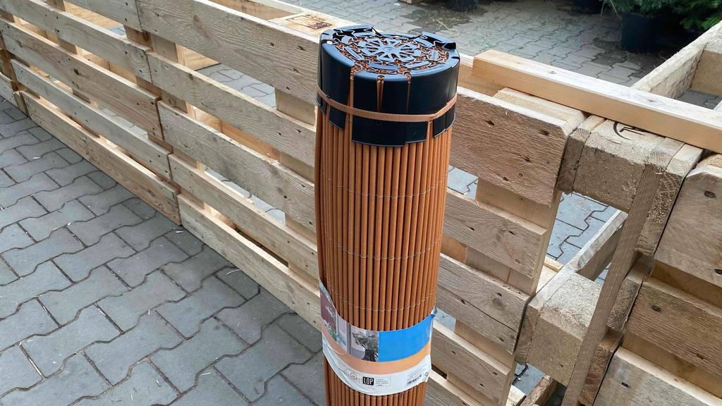 Balkon-Sichtschutz im Test: Balkon-Sichtschutz eingerollt und aufrecht stehend vor Paletten.