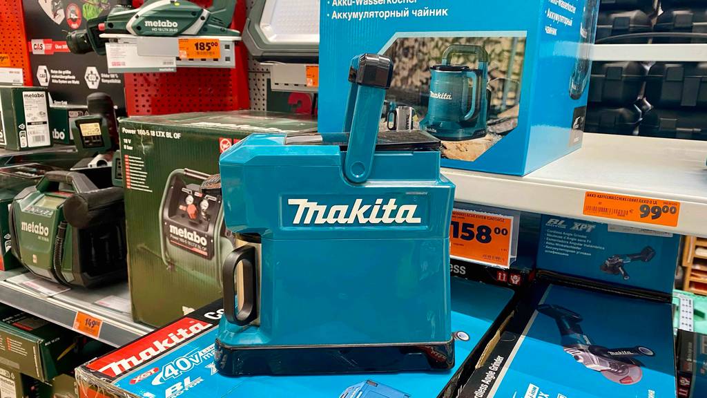 12v-Kaffeemaschine -Test: eine blaue 12v-Kaffeemaschine von Makita steht in einem Regal auf Verpackungen.