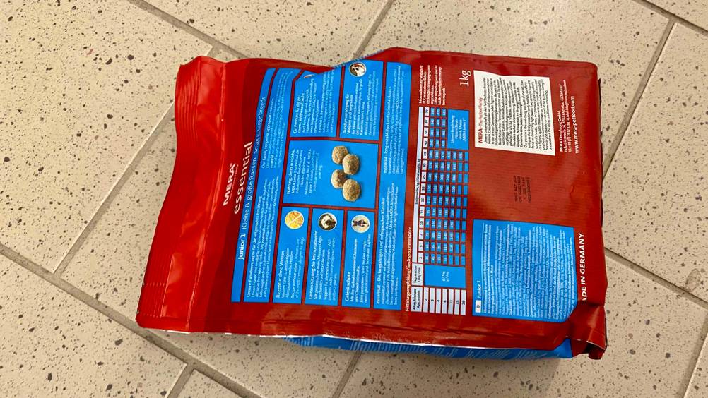 Auf einem hellen Boden liegt eine getestete Packung Welpen-Trockenfutter mit der Rückseite nach oben