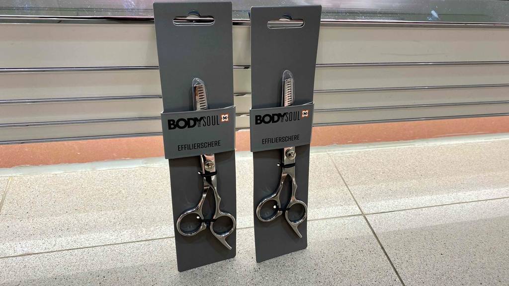 Effilierschere getestet: Zwei verpackte Scheren lehnen nebeneinander an einem Regal.