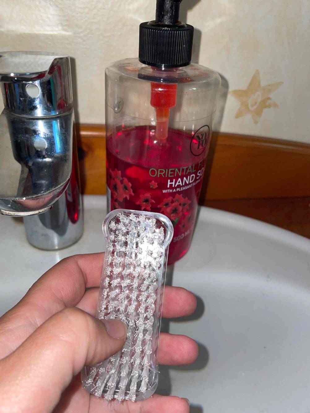 Nagelbürste in der Hand vor einem Waschbecken.