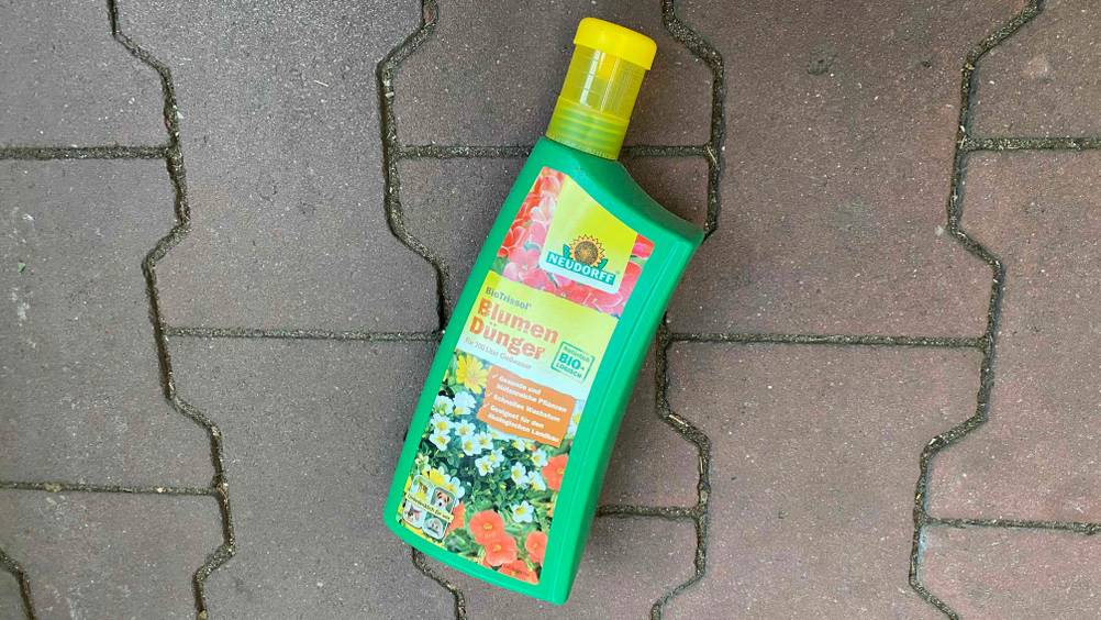 Blumendünger im Test: Eine Flasche Dünger liegt auf Pflasterboden