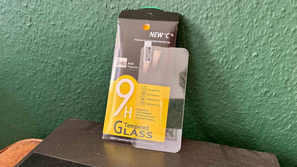 Die Verpackung des getesteten iPhone-13-Pro-Panzerglases lehnt an einer grünen Wand währenddessen das Panzerglas davor platziert ist.