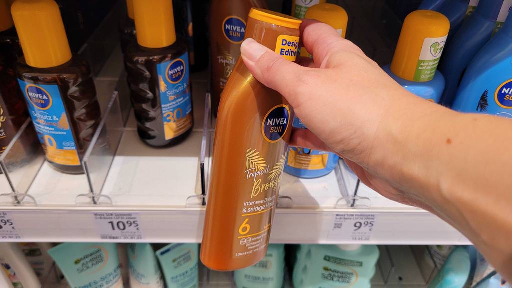 Bräunungsbeschleuniger getestet: eine Flasche Bräunungsbeschleuniger wird vor einem Regal gehalten.