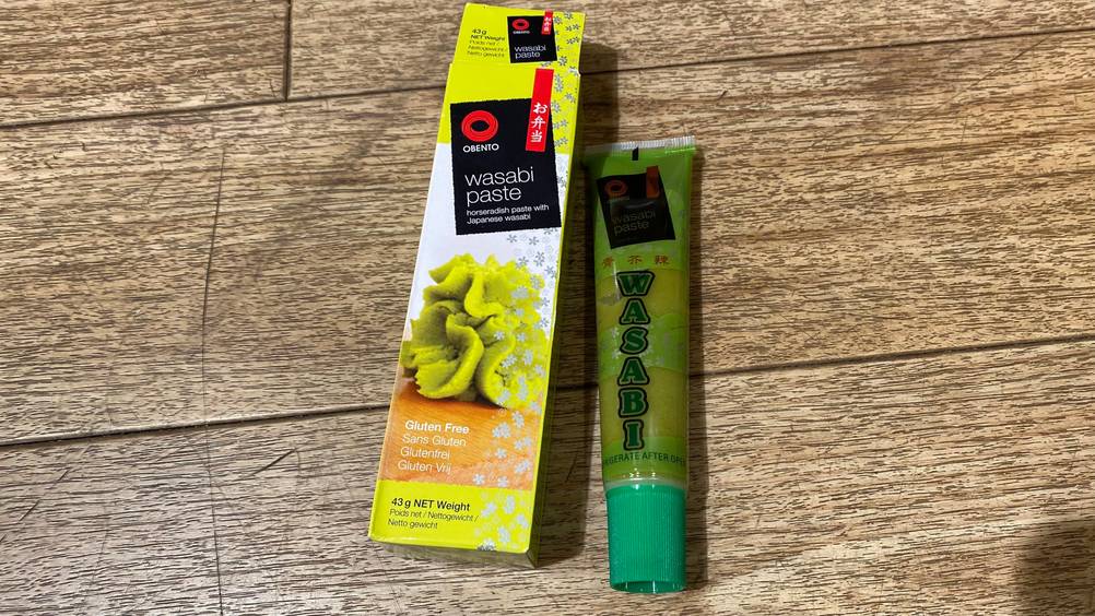 Eine Tube getestete Wasabi-Paste vertikal neben ihrer Originalverpackung.