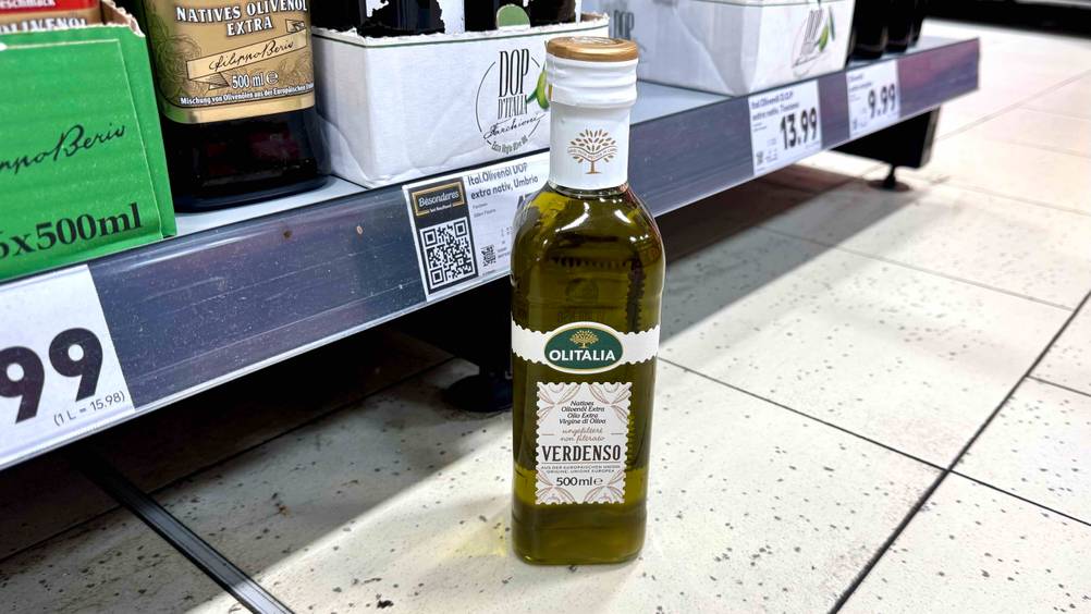 Eine Flasche des getesteten ungefilterten Olivenöls steht vor einem Regal.