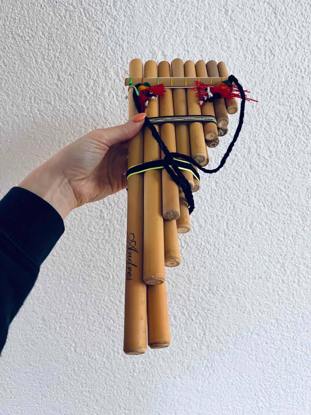 Eine Hand hält eine getestete Panflöte vor eine helle Wand.