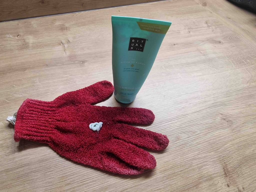 Peelinghandschuh getestet: roter Peelinghandschuh mit Peeling darauf und daneben Peelingprodukt stehend.