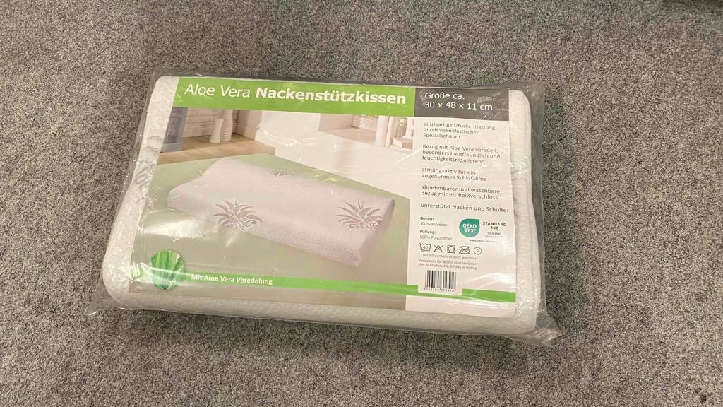 Nackenstützkissen im Test: ein Nackenstützkissen liegend auf einem Boden in der Verpackung mit verschiedenen Informationen zum Produkt.