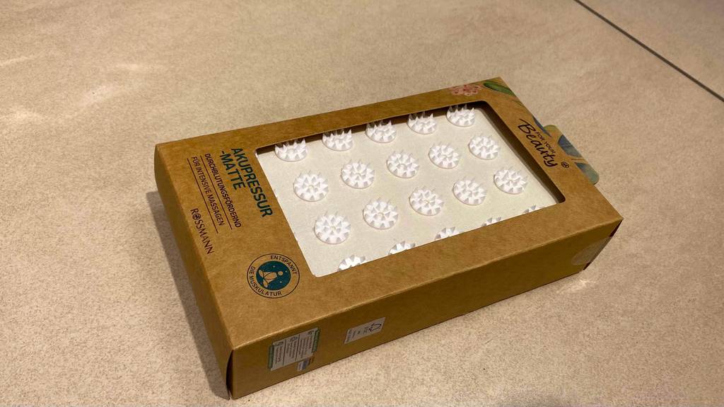 Akupressurmatte getestet: eine Akupressurmatte in der Verpackung, liegend auf einem Boden.