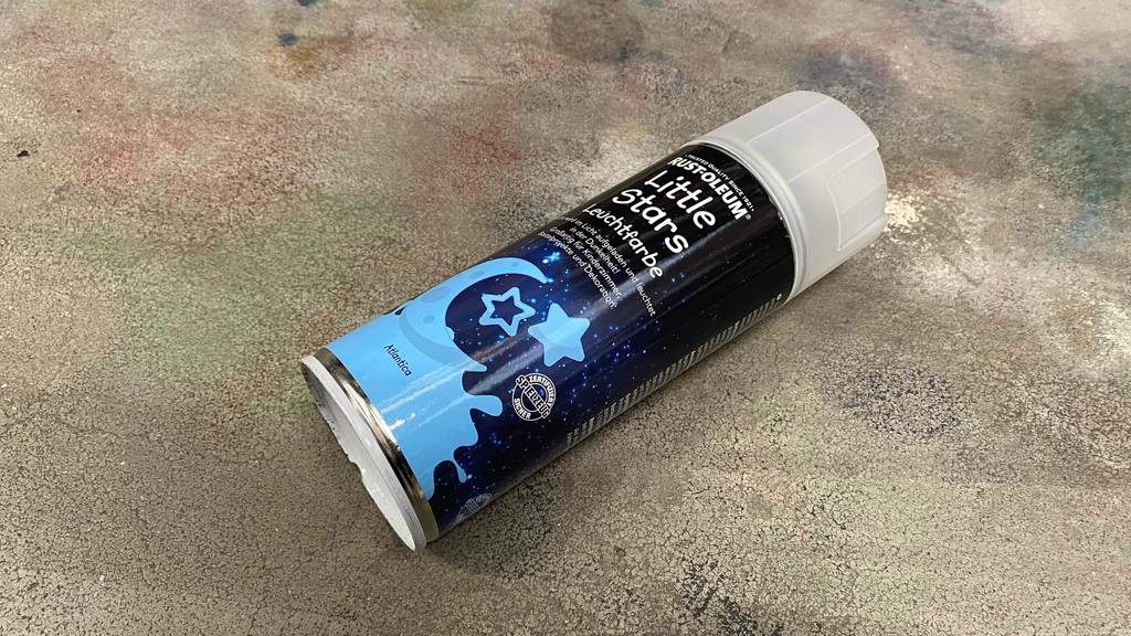 Eine getestete Dose Leuchtfarbe liegt quer auf einem Betonboden.