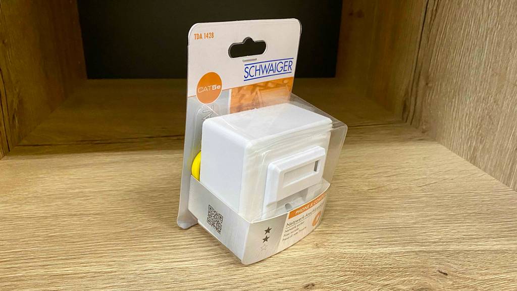 Netzwerkdose getestet: eine Netzwerkdose in der Originalverpackung schräg auf einer Holzfläche platziert.