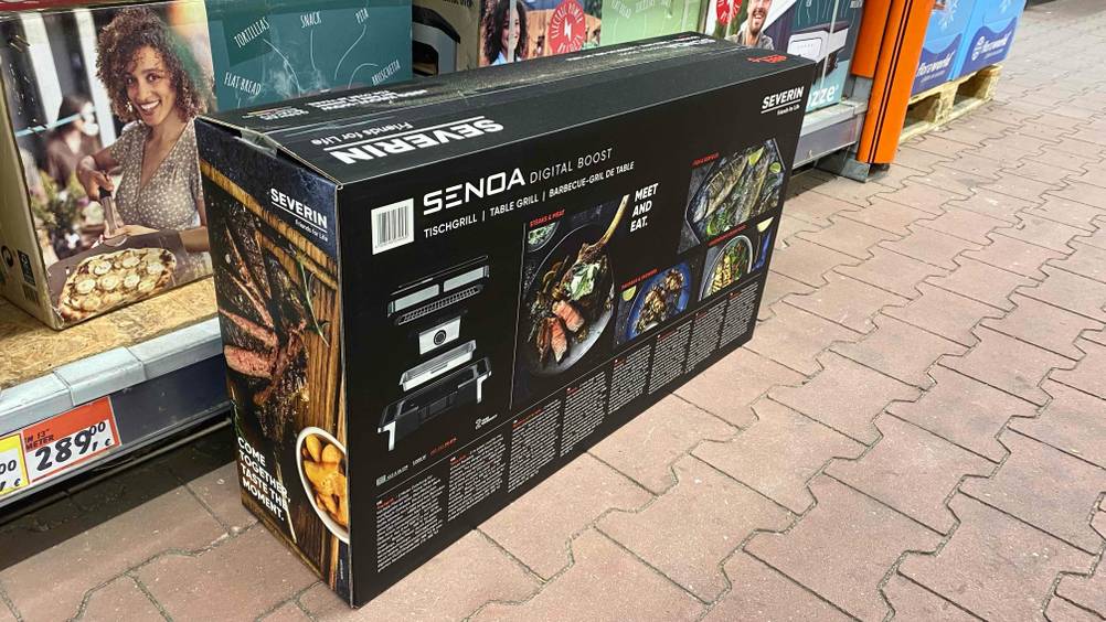 Severin-Elektrogrill im Test: die Verpackung eines Severin-Elektrogrills von der Rückseite ersichtlich, vor einem Regal stehend.