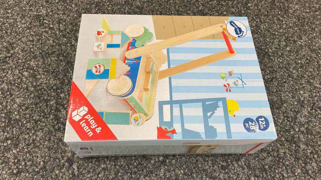 Im Test: Ein verpackter Lauflernwagen aus Holz liegt horizontal auf einem dunklen Boden.