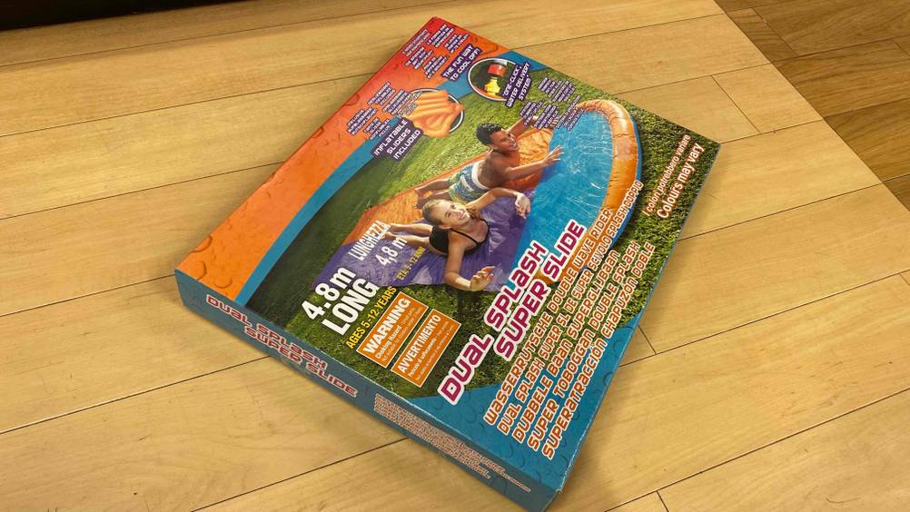 Auf einem Holzboden liegt quer eine getestete Wasserrutsche in Verpackung.