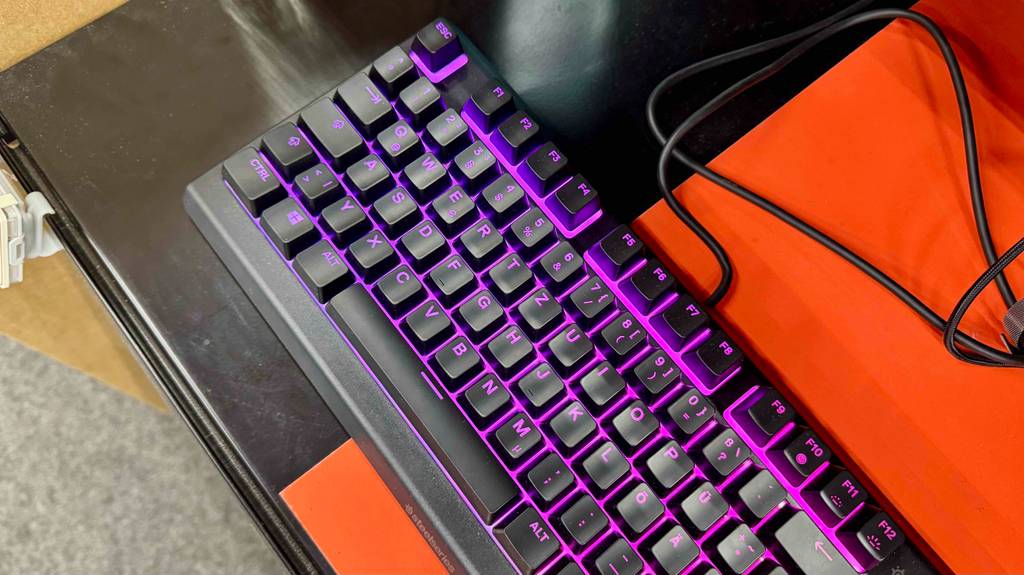 Im Test: Die lila beleuchtete SteelSeries-Tastatur steht auf einem orangefarbenen Tisch.