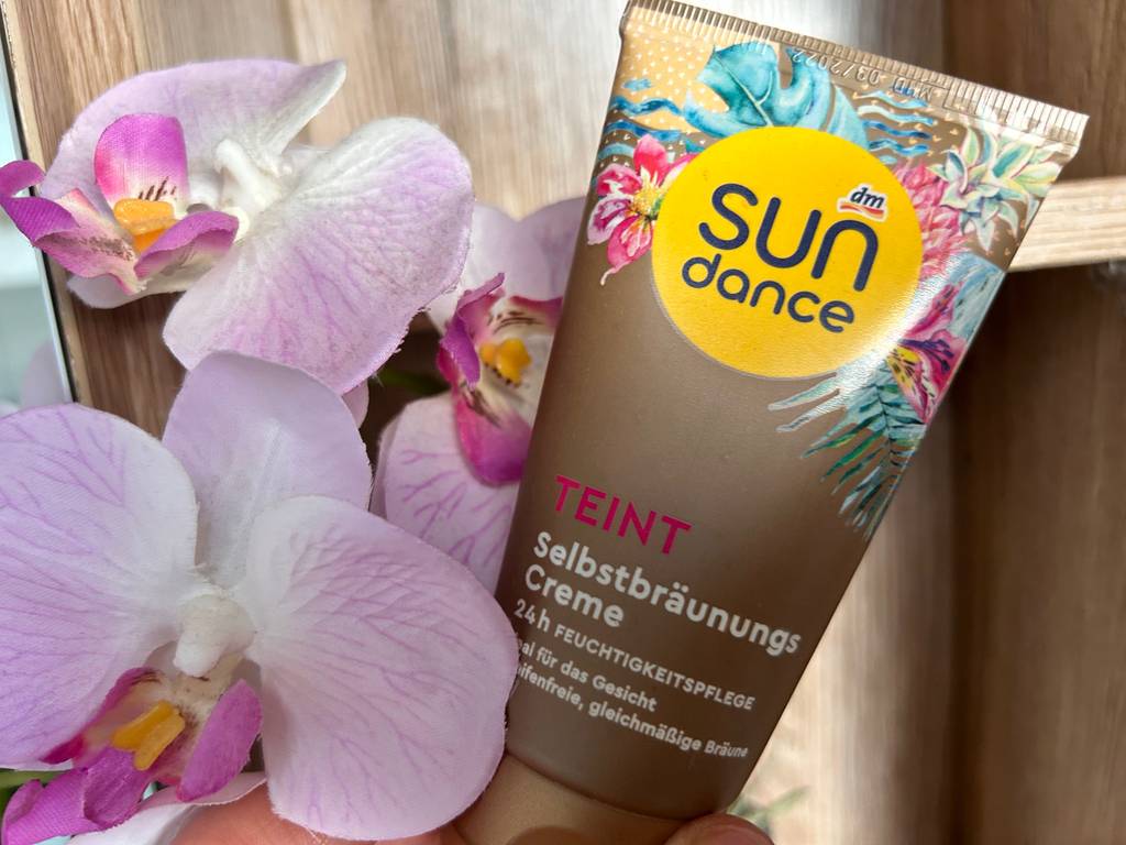 Tube von getestetem Gesichtsbräuner neben einer Orchidee.