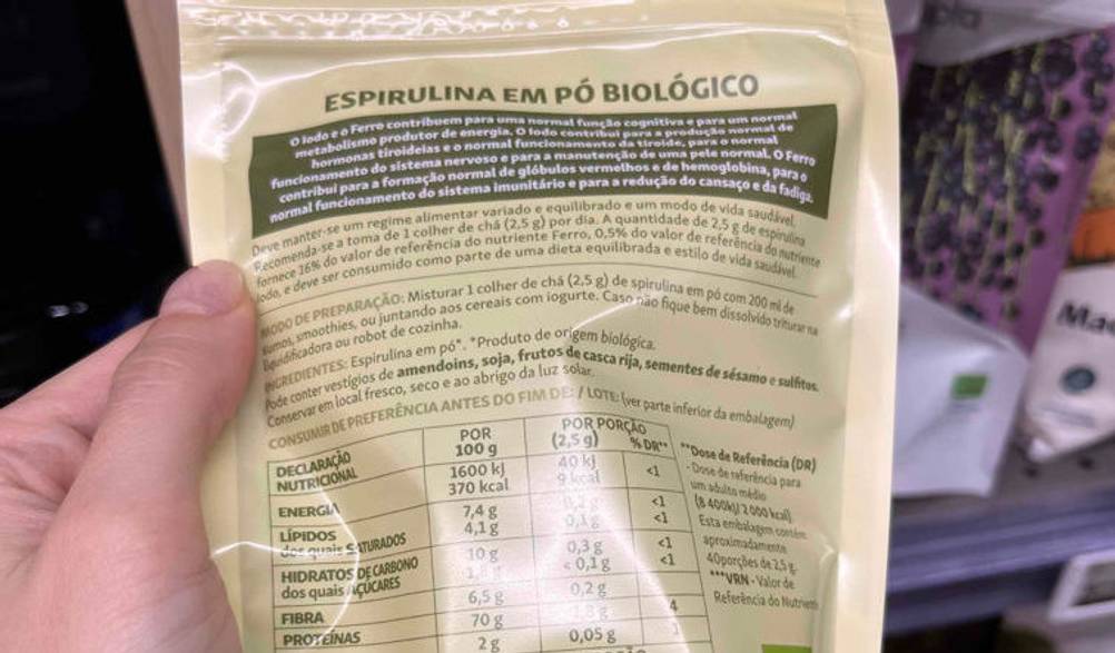 Spirulina getestet: Rückseite von Spirulina-Packung wird in die Kamera vor einem Regal gehalten.