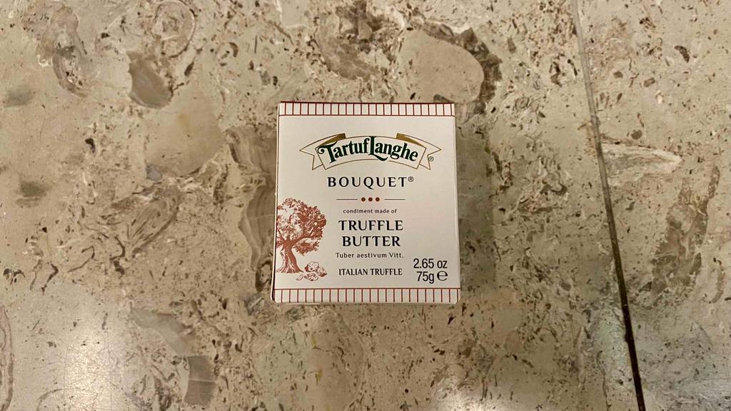 Eine getestete Trüffelbutter in ihrer Originalverpackung liegt auf einer Steinfläche.