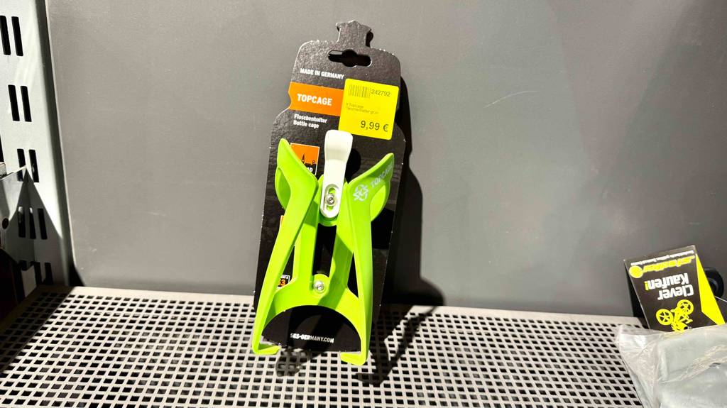 Der getestete Fahrrad-Flaschenhalter in Grün steht auf einem Regal.
