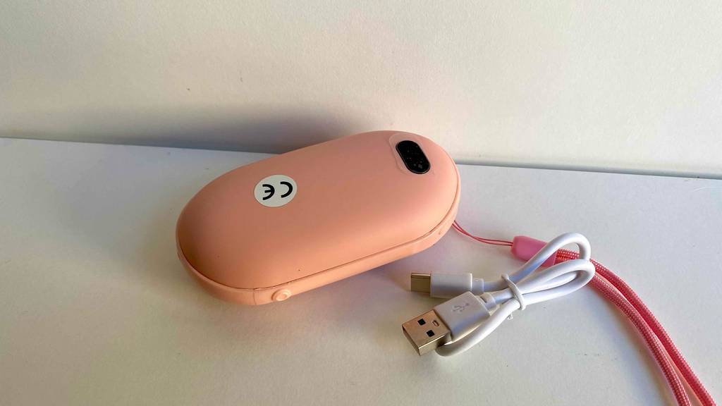 USB-Handwärmer im Test: ein USB-Handwärmer mit dem Netzteil daneben auf einer weißen Fläche liegend.