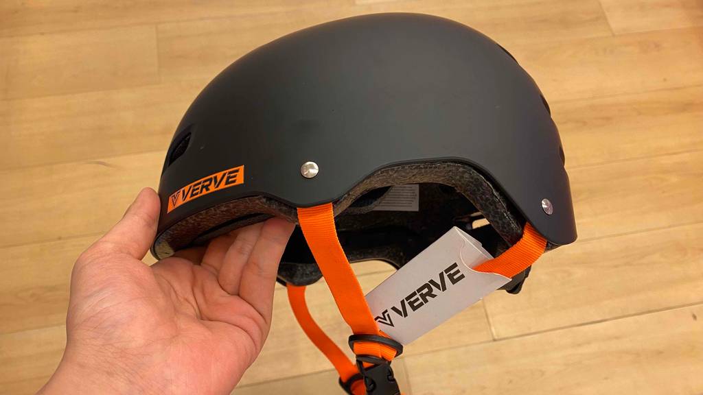 Skaterhelm-Test: schwarzer Skaterhelm mit orangen Bändern wird in der Hand gehalten.