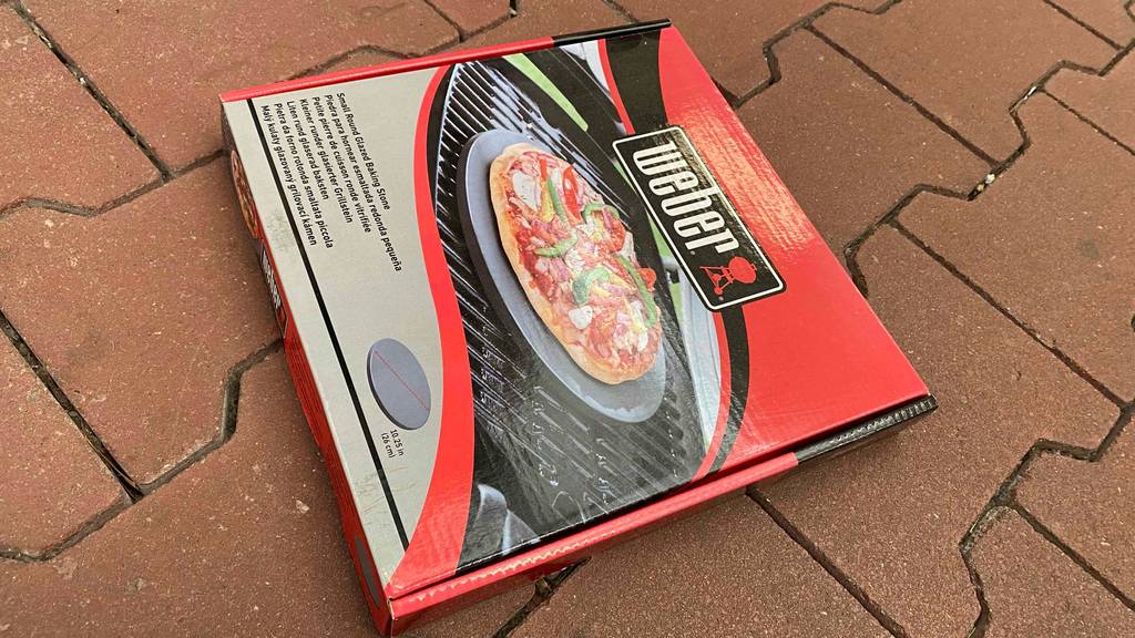 Runder Pizzastein-Test: geschlossene Verpackung von Pizzastein mit einem Durchmesser von 26 cm. auf dem Boden liegend.