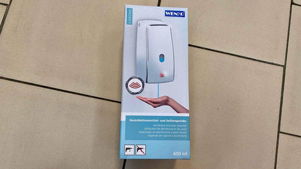 Ein getesteter Seifenspender (Wand) in seiner Verpackung auf einem Fließenboden liegend.