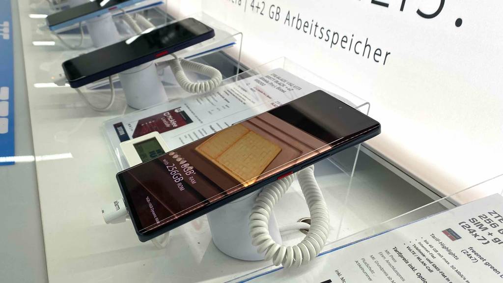 Ein getestetes ZTE-Handy in einer Halterung neben anderern Produkten auf einer hellen Fläche.