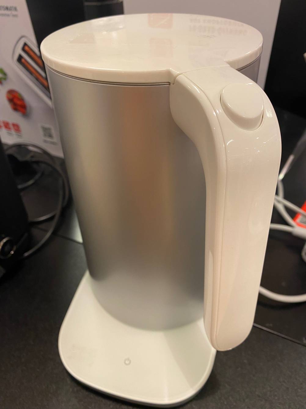 Ein getesteter Design-Wasserkocher mit seinem Henkel nach vorne steht auf einer dunklen Fläche.