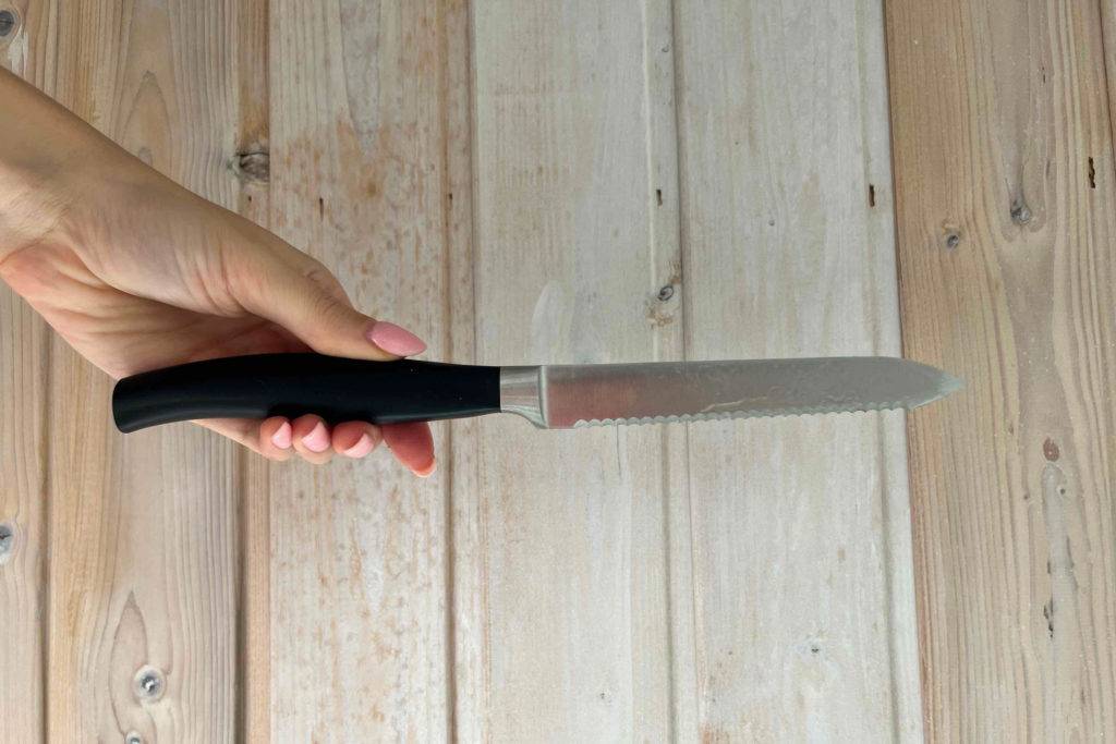 Zwilling-Messer getestet: Eine Hand hält ein Messer am Griff vor eine Holzwand