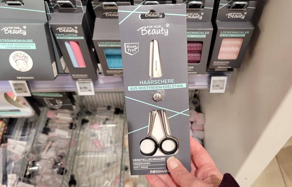 Eine getestete Friseurschere wird in der Hand vor einem Regal gehalten.