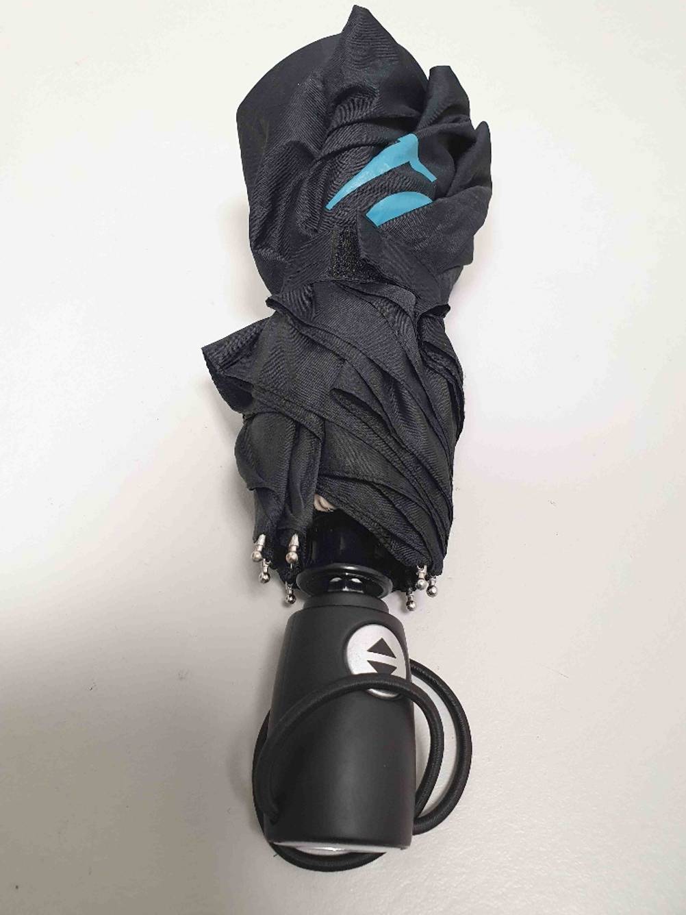 Test: Der schwarze Trekkingschirm im geschlossenen Zustand liegt auf einer weißen Fläche.